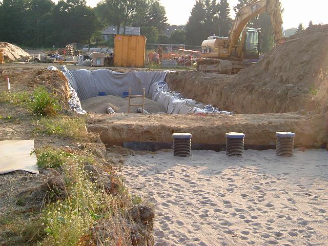 2005_0713_185546.JPG - Große Mulde südl. des Altbestandes - Im Vordergrund eine mit Sand abgedeckte Rigole - Muldenüberlaufschächte - Stauwand - Dahinter wird das nächste Rigolen-Element mit Kies befüllt.